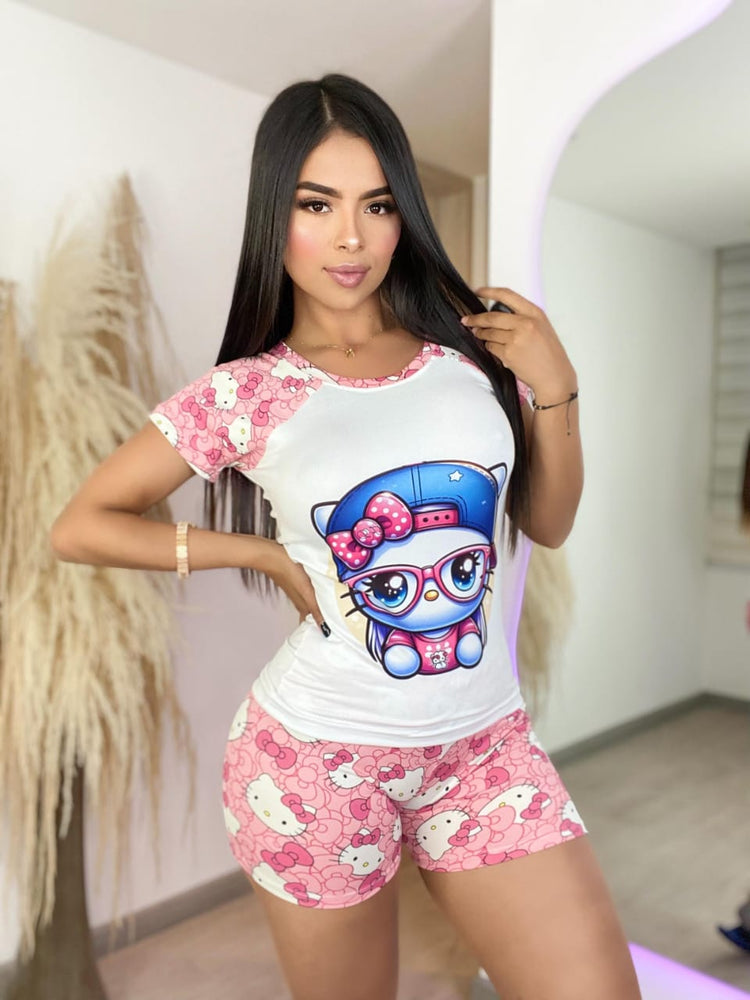 Modelo con maquillaje sutil luciendo un atuendo deportivo o de dormir de Hello Kitty. El conjunto de short y camiseta predomina en colores blanco y rosa, destacando el estampado repetido del personaje y un gran dibujo de Hello Kitty &
