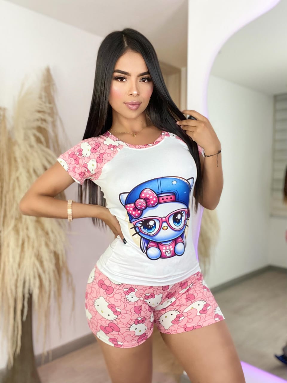 Modelo con maquillaje sutil luciendo un atuendo deportivo o de dormir de Hello Kitty. El conjunto de short y camiseta predomina en colores blanco y rosa, destacando el estampado repetido del personaje y un gran dibujo de Hello Kitty &