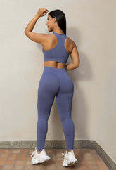 Mujer con conjunto deportivo seamless azul, top push up y leggins moldeadores de lycra texturizada, vista trasera.