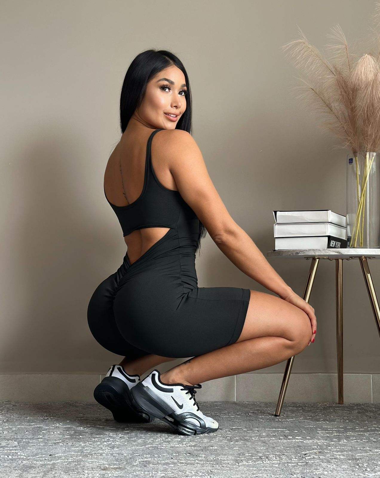Mujer usando enterizo deportivo biker negro con espalda descubierta y ajuste moldeador en posición agachada