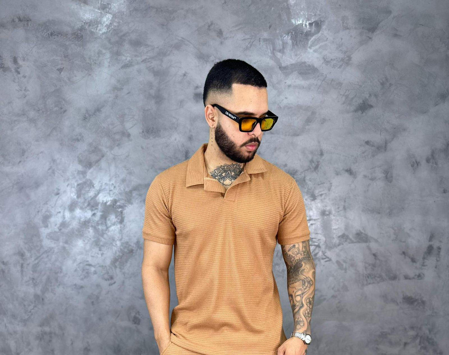 Hombre con camiseta polo texturizada beige de algodón, estilo clásico y moderno, frente a fondo gris
