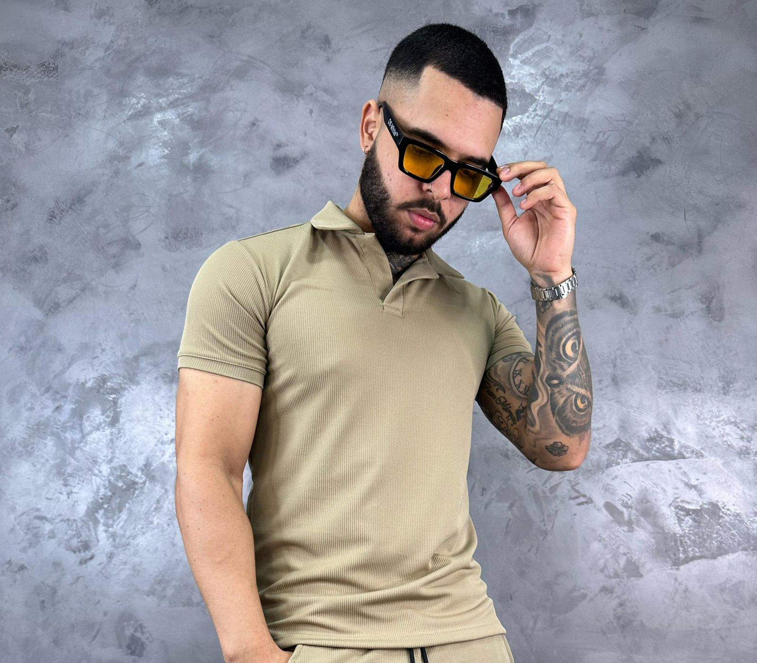 Hombre con camiseta polo texturizada beige de algodón, estilo clásico y moderno, frente a fondo gris