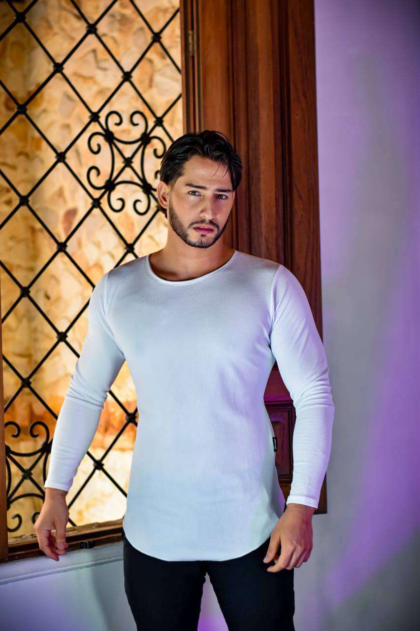 Hombre usando blusa galleta licrada blanca ajustada de manga larga frente a ventana decorativa.