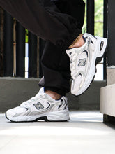 New Balance 530 2.0 Y6 white breathable mesh sneakers with black accents and cushioned sole on person wearing black pants