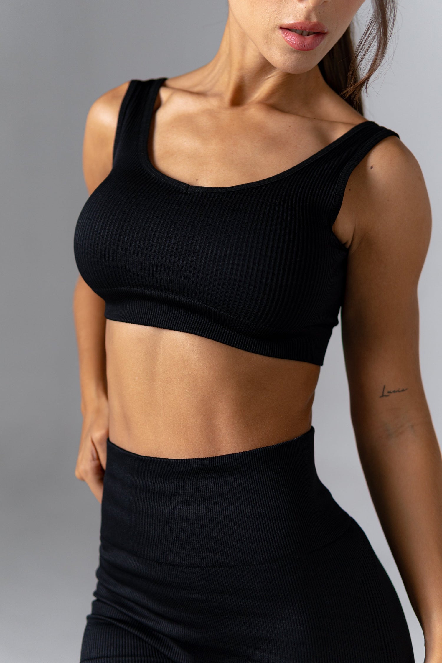 Mujer usando conjunto deportivo seamless negro push up con top y short, con mancuernas rosas y botella de agua negra.