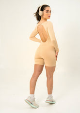 Mujer usando enterizo corto seamless beige SKINFLEX sin costuras con espalda descubierta y auriculares.