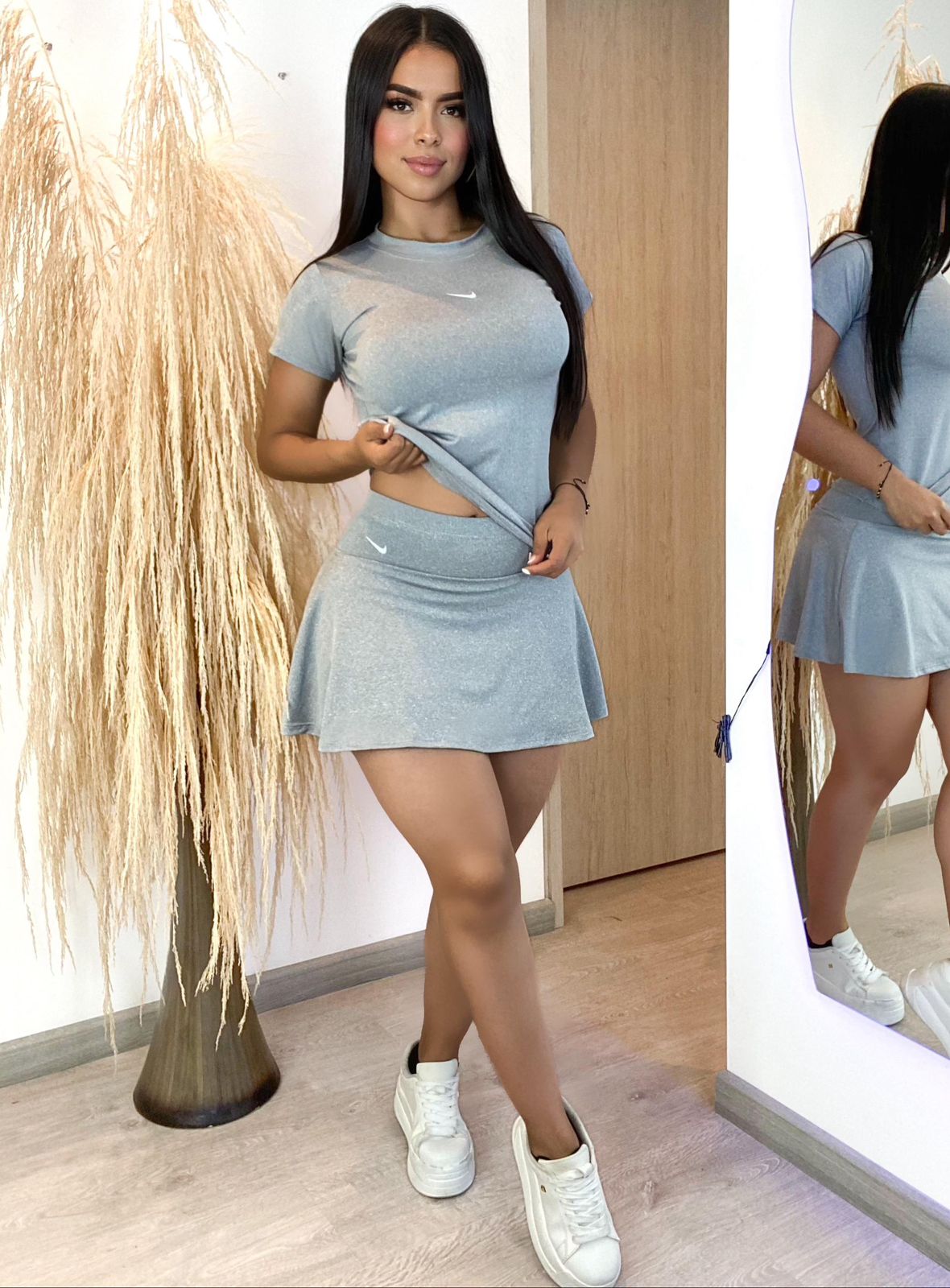 Mujer con conjunto falda short deportivo casual gris, camiseta crop y zapatillas blancas, ambiente interior moderno