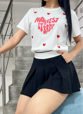 Camiseta de corazones blanca con estampado rojo y falda negra plisada, estilo casual y moderno